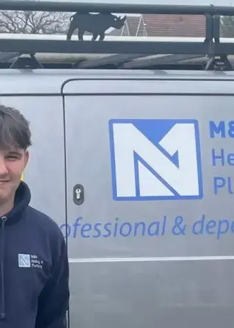 Apprentice standing in front of a MN plumbing and heating van thats grey