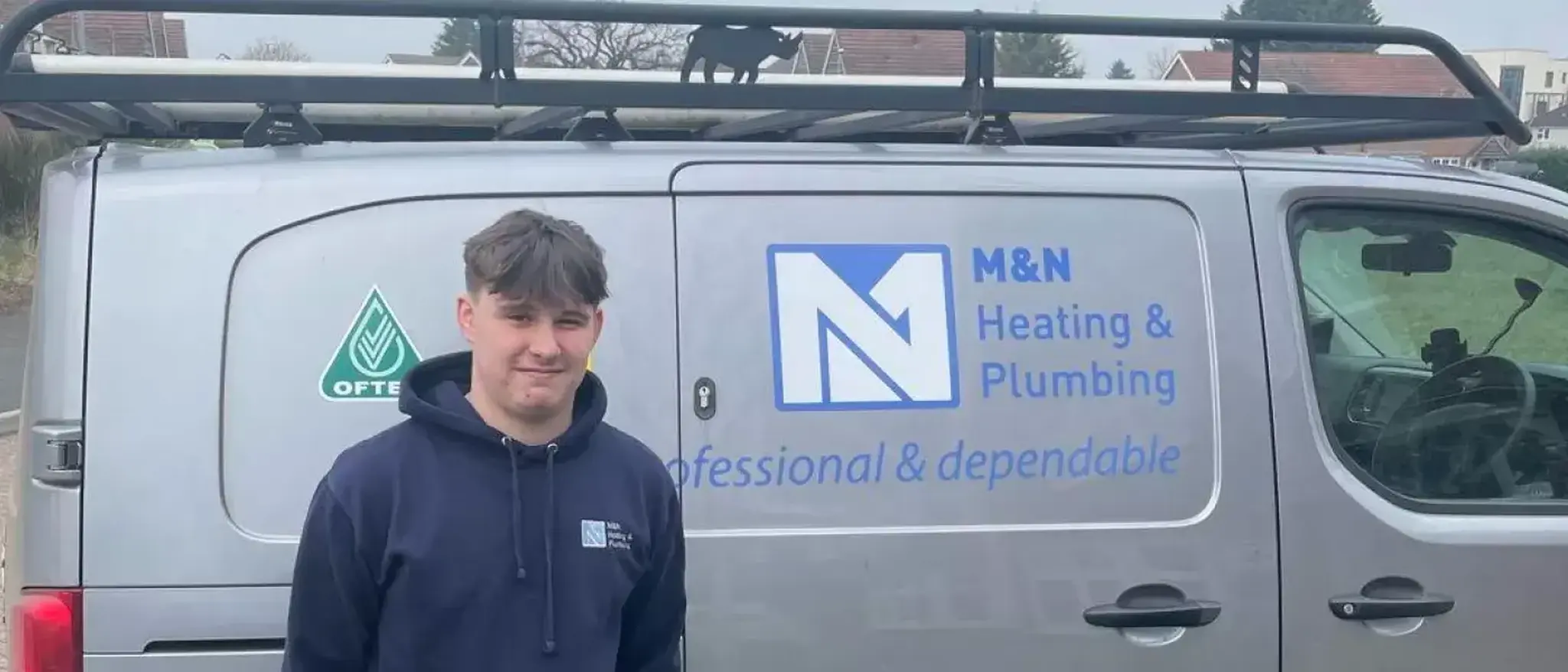 Apprentice standing in front of a MN plumbing and heating van thats grey