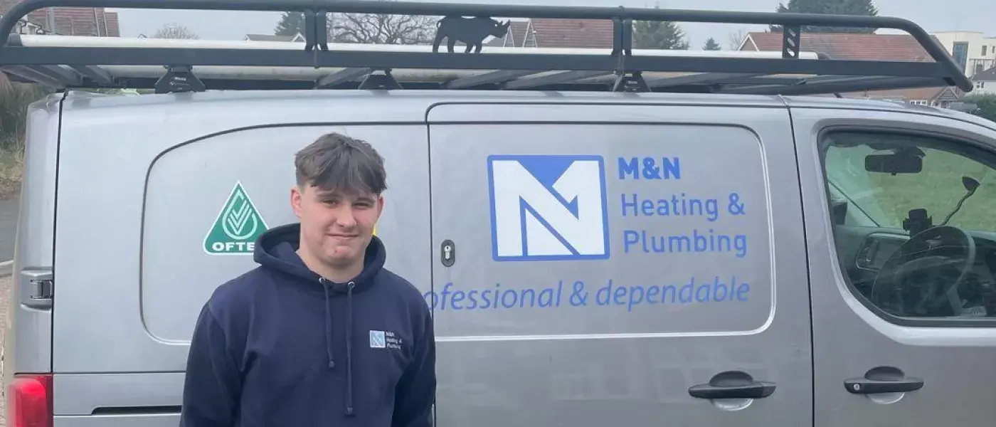 Apprentice standing in front of a MN plumbing and heating van thats grey